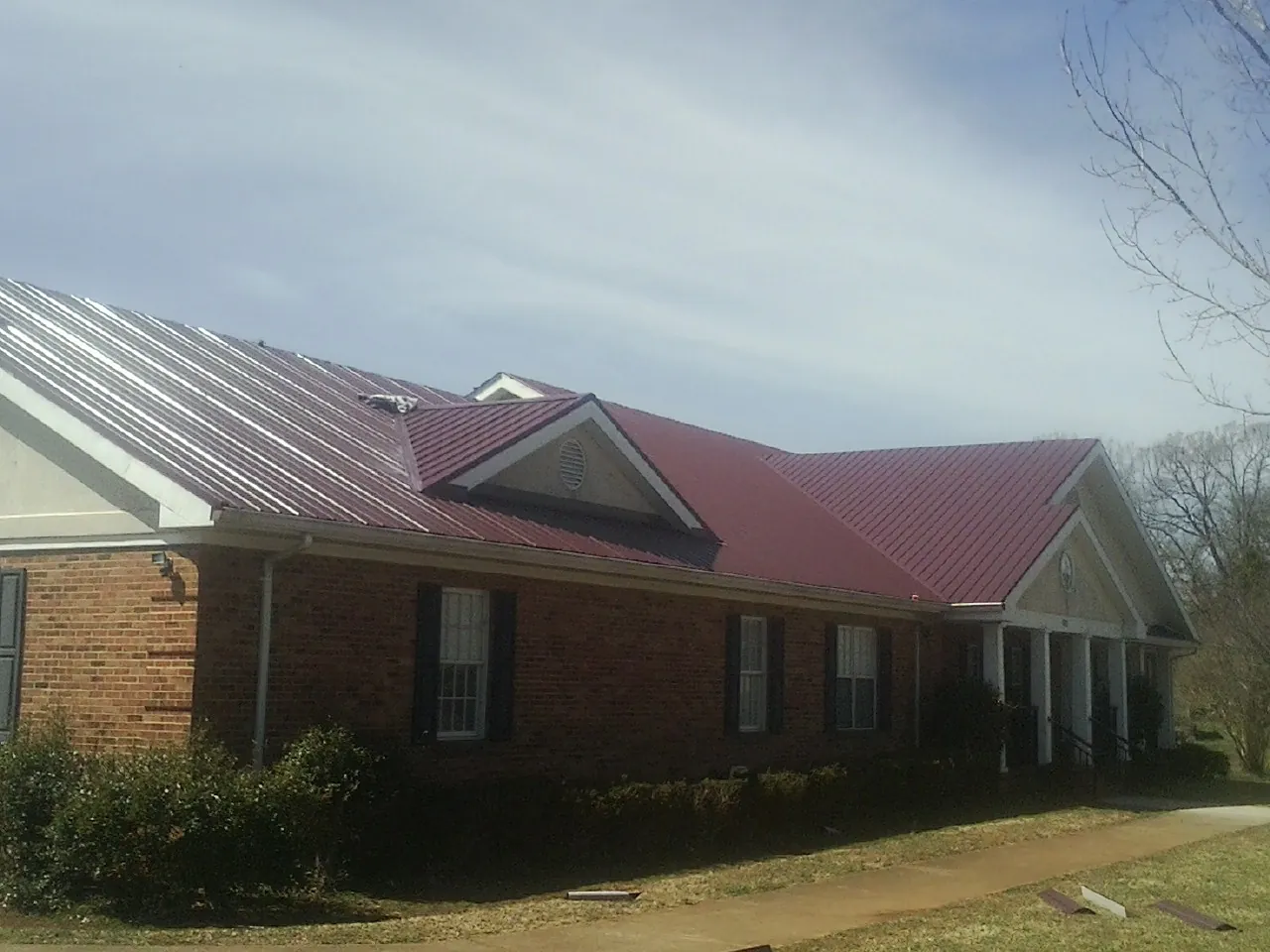 Red metal roof with gabled entries on a long brick building, from a Hail Damage Roof Repair job in Birdsboro