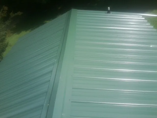 New green metal panels meeting at the ridge of a roof — Flat Roof Repair work by our crew in Birdsboro