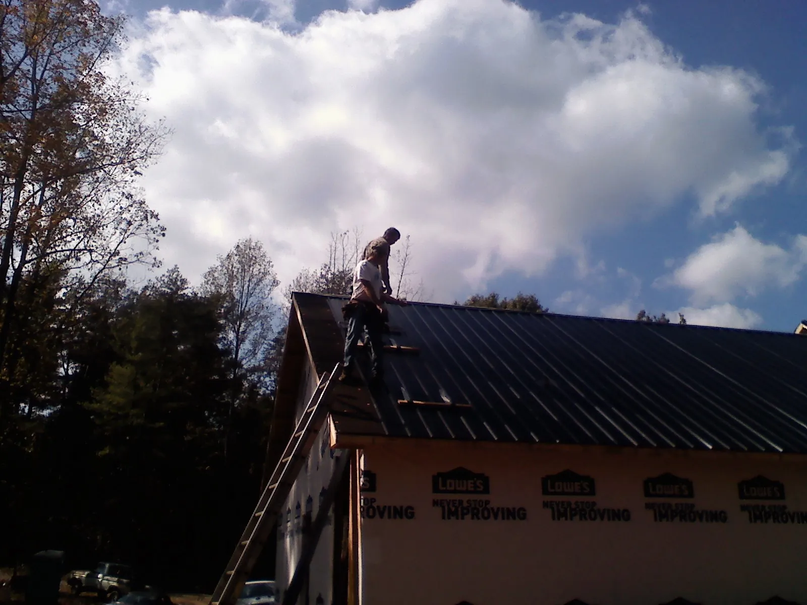 Roofer fastening dark metal panels high against a cloudy sky, from a Roof Inspection job in Birdsboro