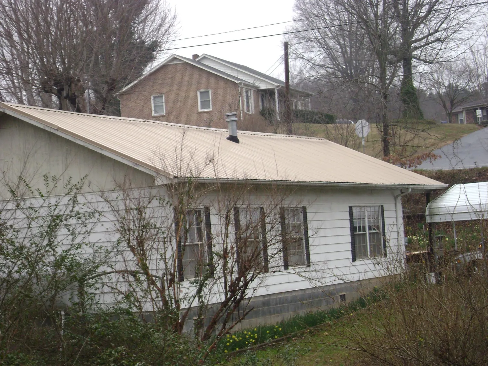 Tan metal roof on a white sided house set into a hillside — Commercial Roofing by Roofing Brothers in Birdsboro